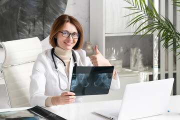 Portrait photo of young and beautiful female doctor in white medical gown sitting and working on...