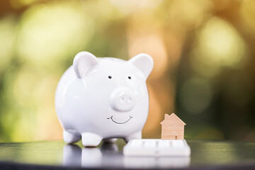 Piggy bank and home model put on the calculator with presenting put on the wood in the public park, Saving money for buy house or loan for investment of real estate concept.