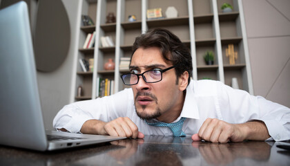 Shocked businessman hiding behind desktop and looking at laptop in the office. Business crisis and...