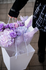 Female hands hold a large bouquet of purple flowers in a gift box-bag