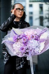 Focus on a large bouquet of purple flowers in the hands of a young pretty woman