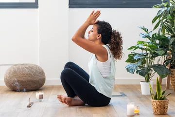 Poster Sporty young woman doing yoga exercises while staying in lotus position in living room at home. © nenetus
