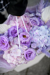 Top view close-up of a large bouquet of purple flowers held by female hands in a gift bag-box