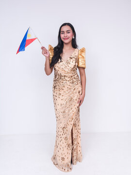 Elegant Filipino woman in a champagne Filipiniana dress holding the Philippine flag