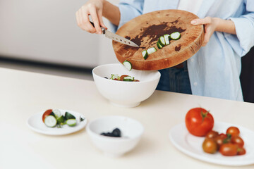 Woman preparing healthy vegetable salad on wooden cutting board with bowl of salad