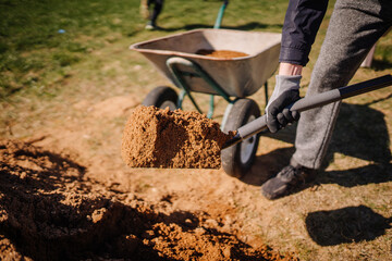 Valmiera, Latvia - April 21, 2024 - A person is shoveling soil into a wheelbarrow on a sunny day,...