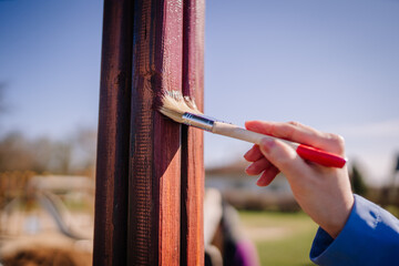 Valmiera, Latvia - April 21, 2024 - A close-up of a hand painting a wooden beam with a brush, in...