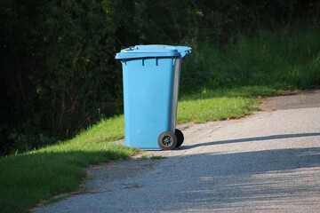 Large blue plastic trash can for waste paper stands alone on the side of the road, waiting to be picked up