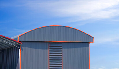 Large gray aluminium industrial warehouse building with curve roof next to pavilion against blue...