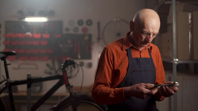 Old man mechanic repairing a bicycle standing with adjustable wrenches in his hands looking at the camera. repairing modern bike using special tool