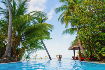 A woman enjoys summer vacation in a swimming pool under the palm trees.