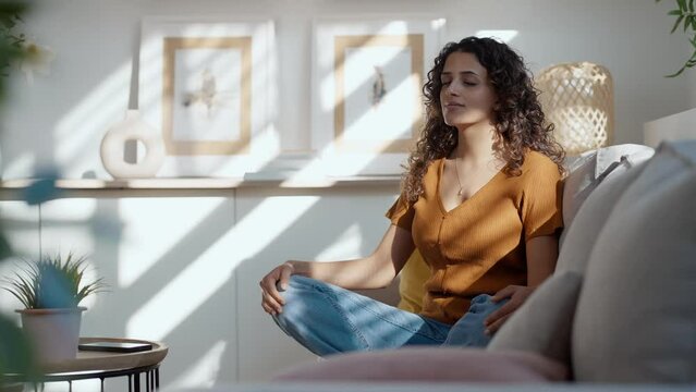 Video of  pretty young woman in lotus position sitting on the sofa at living room at home.