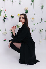 Vertical photo of young woman poses near flowers hanging in air on white background. Photo studio location for photoshoot
