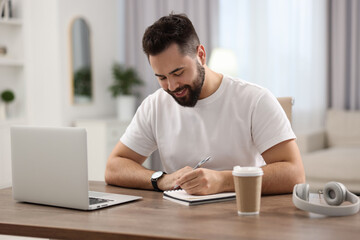 Young man writing down notes during webinar at table in room