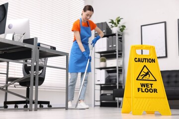 Cleaning service worker washing floor with mop in office, focus on wet floor sign