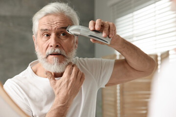 Senior man trimming eyebrows near mirror in bathroom