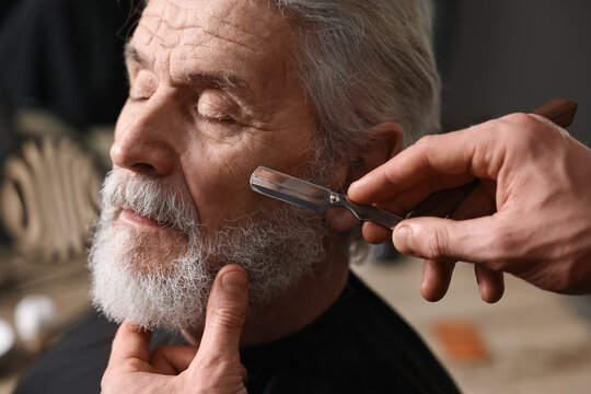 Fototapeta Professional barber shaving client's beard with blade in barbershop