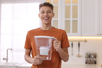 Happy man with water filter jug in kitchen