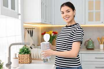 Woman holding filter jug with water in kitchen