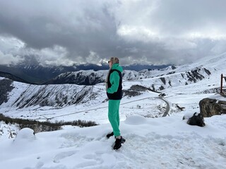A woman on the background of the Ceylomsky pass in Ingushetia. A trip uphill to the Tsei Lum pass on a cloudy spring day. Panorama of the high cliffs of the Dzheyrakh gorge