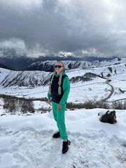 A woman on the background of the Ceylomsky pass in Ingushetia. A trip uphill to the Tsei Lum pass on a cloudy spring day. Panorama of the high cliffs of the Dzheyrakh gorge