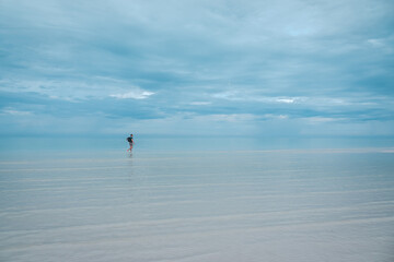 Fototapeta na wymiar Solitary Figure Walking in Calm Seaside Waters in Holbox in Mexico