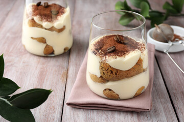 Delicious tiramisu with coffee beans in glasses and green leaves on wooden table