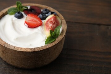 Bowl with yogurt, berries, fruits and mint on wooden table, closeup. Space for text