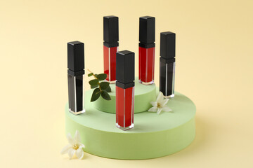 Different lip glosses, podiums and flowers on beige background