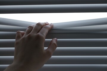 Woman separating slats of white blinds indoors, closeup