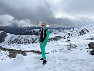 A woman on the background of the Ceylomsky pass in Ingushetia. A trip uphill to the Tsei Lum pass on a cloudy spring day. Panorama of the high cliffs of the Dzheyrakh gorge