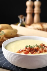 Tasty potato soup with bacon and rosemary in bowl on table, closeup