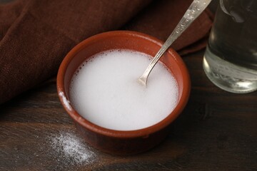 Chemical reaction of vinegar and baking soda in bowl on wooden table, closeup