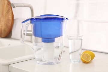 Water filter jug, glass and lemons on countertop in kitchen