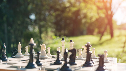 Sunlit chess pieces on board in natural setting, strategic gameplay captured. Light casts shadows...