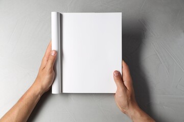 Man holding blank notebook at light grey table, top view. Mockup for design