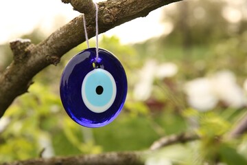 Evil eye amulet hanging on blossoming spring tree outdoors, closeup. Space for text