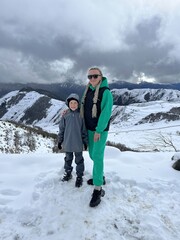 A woman with a child on the background of the Ceylomsky pass in Ingushetia. A trip uphill to the Tsei Lum pass on a cloudy spring day. Panorama of the high cliffs of the Dzheyrakh gorge