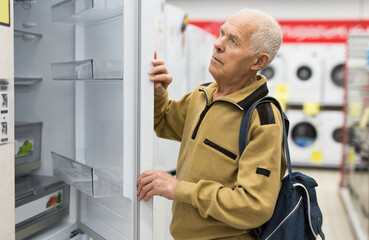 Senor man pensioner buying fridge in showroom of electrical appliance store