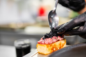 A chef meticulously garnishing a gourmet dish with black caviar, showcasing the artistry and...