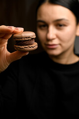 Focus on brown macaroon with chocolate cream with golden stripe in hands of young female pastry chef