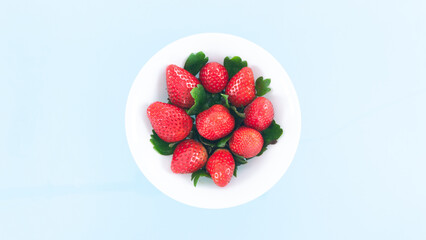 White plate is filled with beautiful juicy red strawberries with beautiful green leaves. Summer...