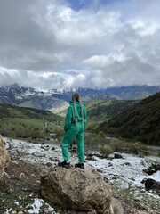 A woman on the background of the Ceylomsky pass in Ingushetia. A trip uphill to the Tsei Lum pass on a cloudy spring day. Panorama of the high cliffs of the Dzheyrakh gorge