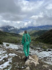 A woman on the background of the Ceylomsky pass in Ingushetia. A trip uphill to the Tsei Lum pass on a cloudy spring day. Panorama of the high cliffs of the Dzheyrakh gorge