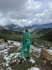 A woman on the background of the Ceylomsky pass in Ingushetia. A trip uphill to the Tsei Lum pass on a cloudy spring day. Panorama of the high cliffs of the Dzheyrakh gorge