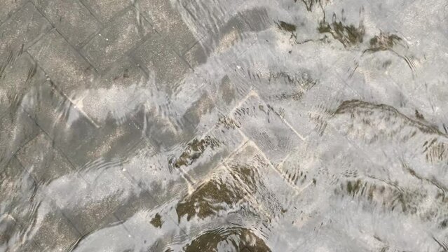 Top view or flat lay view of shallow water flow on grey paved background, flood on the street