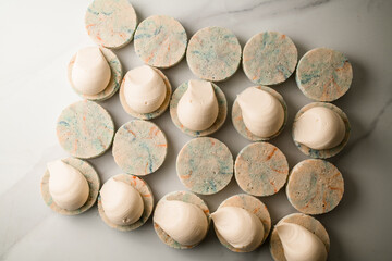 White halves of macaroons lie on a white table with white cream applied