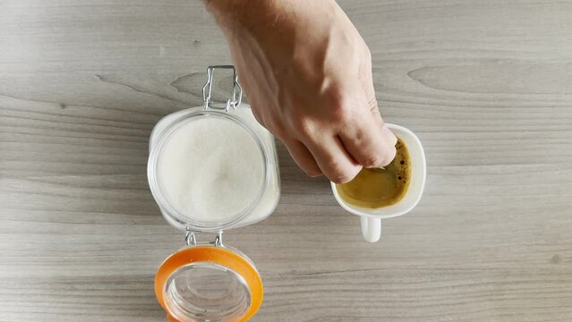 Hand adding a teaspoon of sugar to fresh brewed black coffee