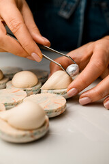 Confectioner's female hands decorate a white macaroon with cream with a silver pistachio nut
