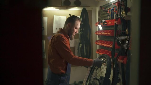 Bike mechanic repairs bicycle in workshop. Man examines and fixes wheel. Bike maintenance
